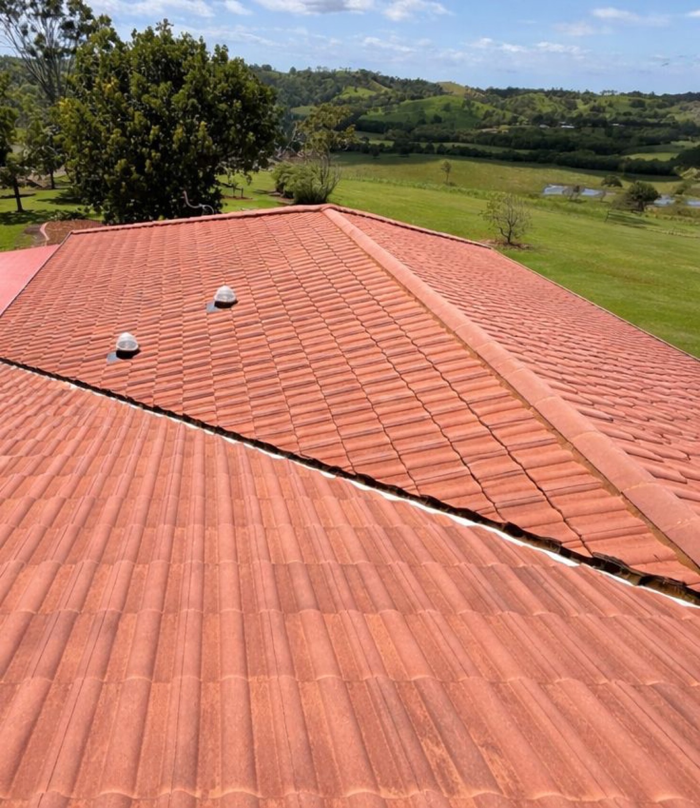 A clean terracotta tile roof on a rural property with green hills behind