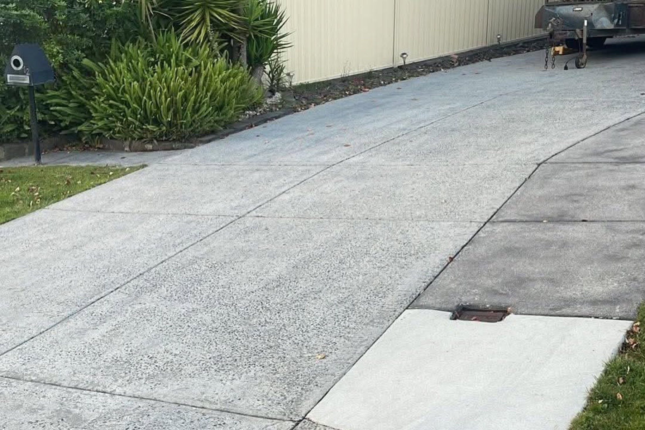 A concrete driveway beside a garden bed with a trailer parked nearby