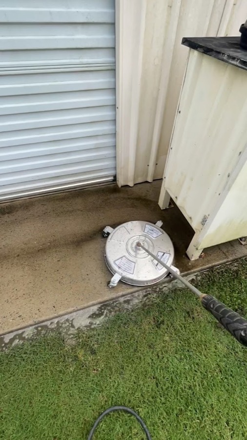 A rotary surface cleaner spraying a concrete driveway