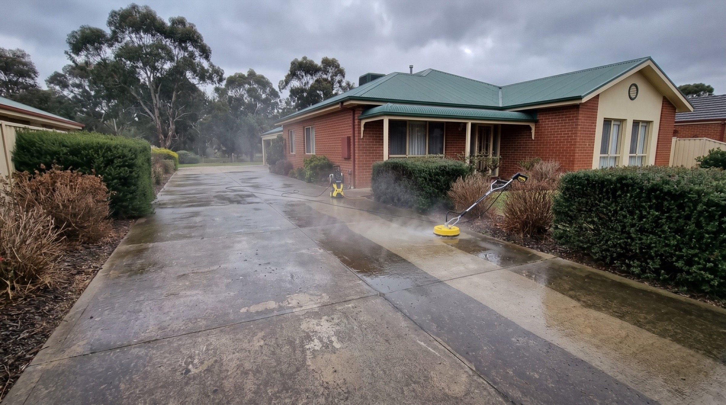 A red brick house with a green roof and a surface cleaner and hose reel on the driveway