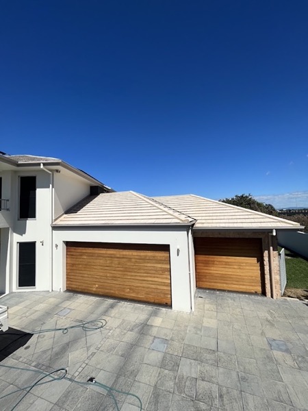 A two-storey rendered house with dark timber-look garage doors at dusk