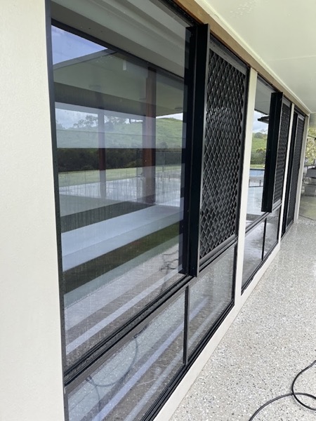 A row of clean windows and security screens with reflections of a pool and hills