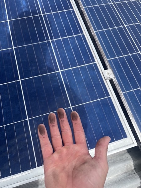 A hand marked with grime resting beside a solar panel