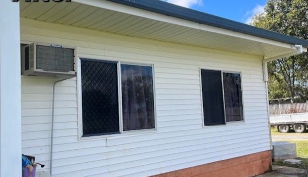 A house exterior wall with an air-conditioning unit and window screens