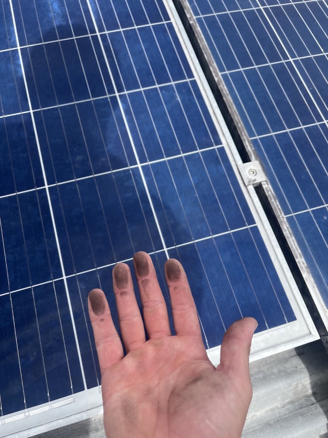 A hand marked with grime resting beside a solar panel