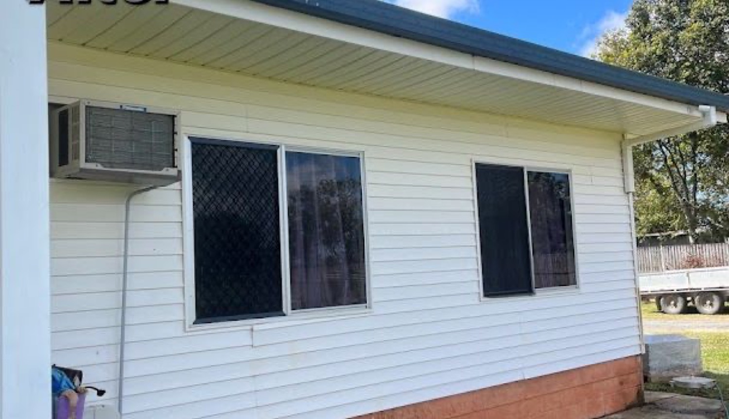 A house exterior wall with an air-conditioning unit and window screens